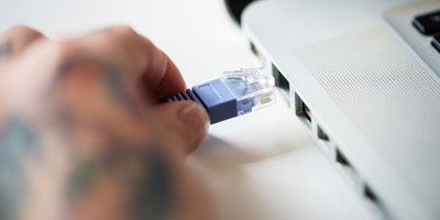 A hand plugging an ethernet cable into a computer