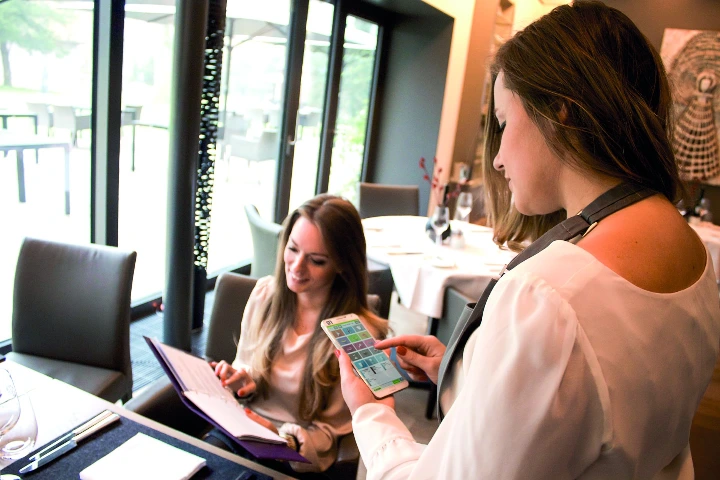 A restaurant server using a mobile handheld device to take an order from a customer, demonstrating Gastronovi’s integrated mobile POS and cloud-based service solution.