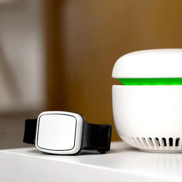  CARU care emergency wristband on a white table next to the glowing green base station device.