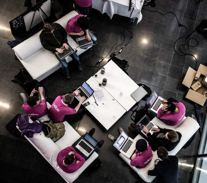 Foto dari atas dari tim Odoo yang sedang bekerja menggunakan komputer mereka.